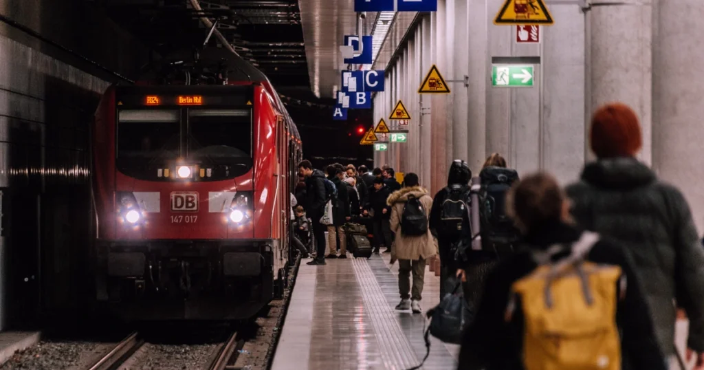 A busy train platform with passengers boarding a red DB train, highlighting the travel experience of taking a train from Lisbon to Madrid.