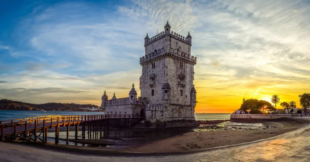 A historic tower in Lisbon, Portugal, at sunset, with a wooden bridge and a vibrant sky, showcasing one of the best cities to visit in Portugal.