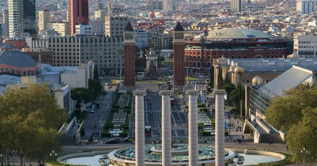 A panoramic view of Plaça d'Espanya in Barcelona, Spain, with iconic Venetian Towers, the Magic Fountain, and a vibrant urban backdrop, showcasing the beauty of Spain and Portugal.