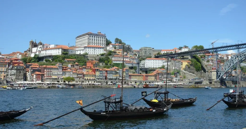 Traditional boats on the Douro River with a view of the colorful historic Ribeira district and Luís I Bridge in Porto, showcasing the cultural charm of Spain and Portugal.