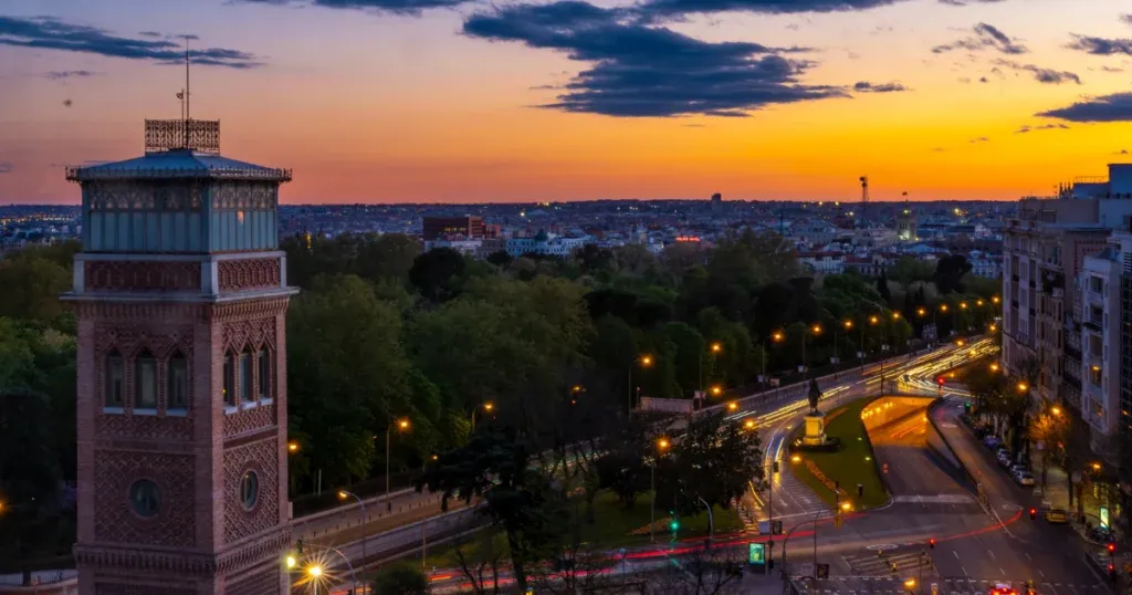 A sunset view of Madrid, featuring a historic tower, glowing city lights, and scenic streets—an ideal setting for the best place to stay in Madrid.