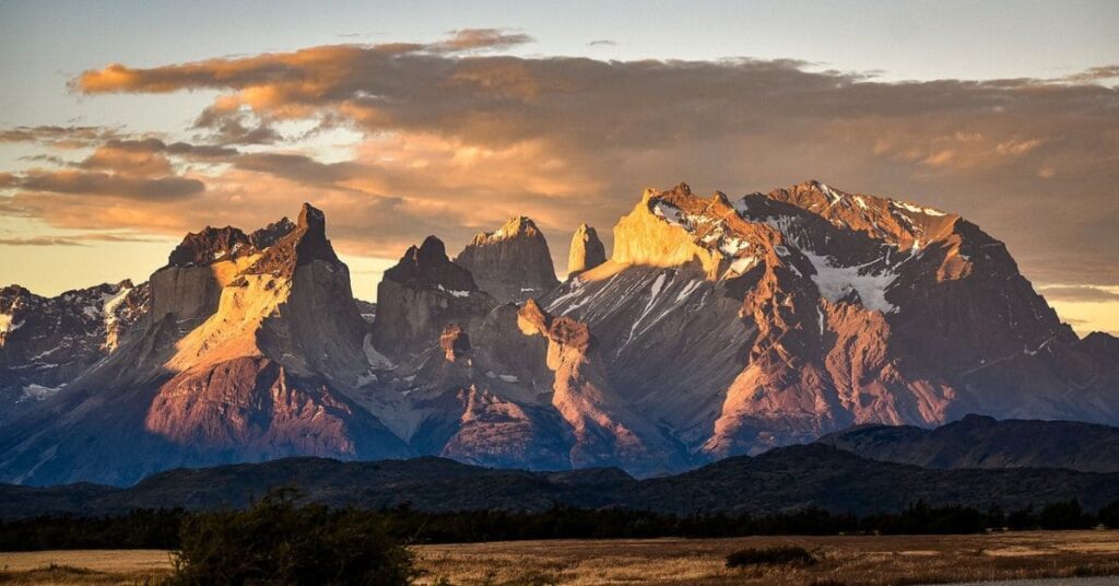 A stunning view of Patagonia's mountains under an orange sky, with rugged peaks and tranquil valleys bathed in warm hues.