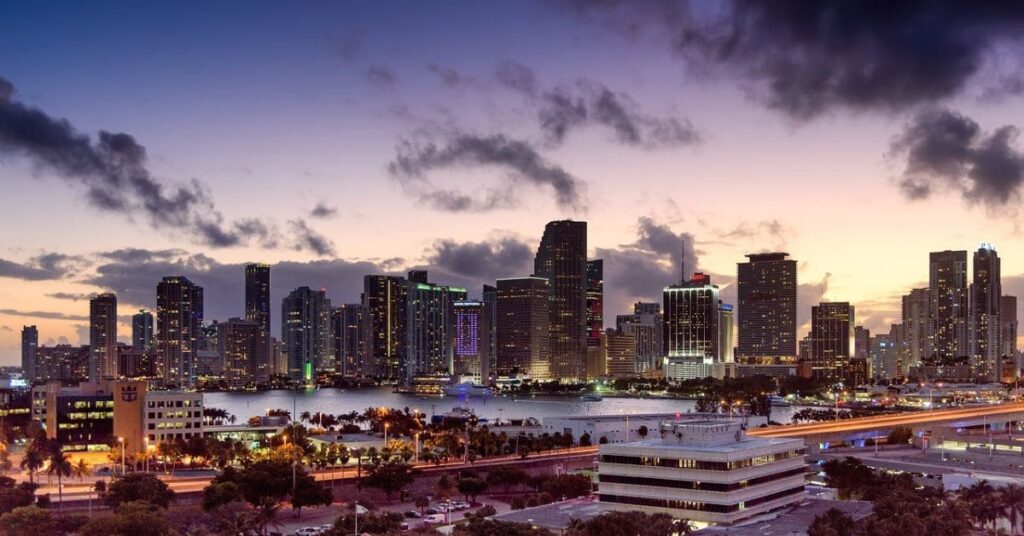 A vibrant evening view of the Miami skyline with illuminated skyscrapers and a dramatic sky in the background, reflecting the allure of one of the best places to visit in March in the USA.