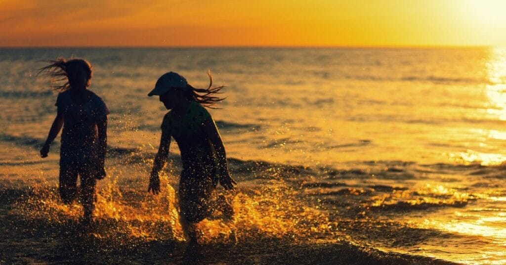 Two children playing in the waves at Orange Beach, Alabama, during a golden sunset, highlighting fun things to do in Orange Beach, Alabama.