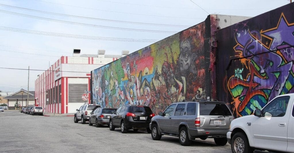 A vibrant graffiti mural on an urban street in Los Angeles, highlighting one of the once in a lifetime things to do in Los Angeles, with parked cars and a striped warehouse in the background.