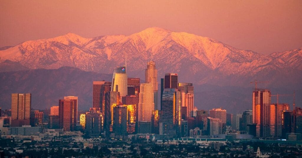 Downtown Los Angeles skyline with the snow-capped San Gabriel Mountains illuminated by a stunning sunset.