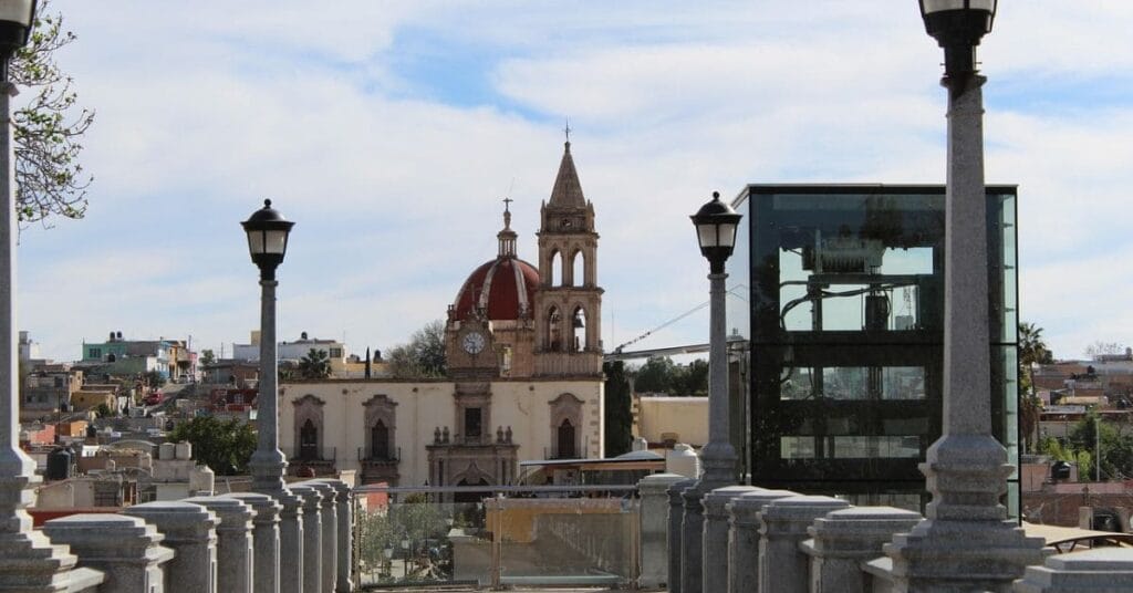 Historic church and cityscape view with a modern glass elevator in the foreground.