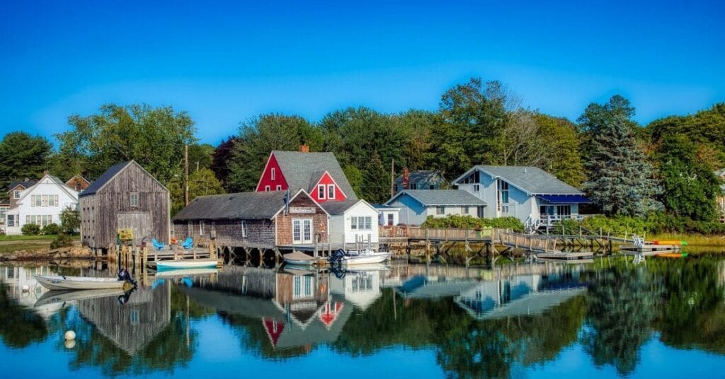 Charming waterfront houses and boats reflected in calm water under a bright blue sky in Kennebunkport, Maine.