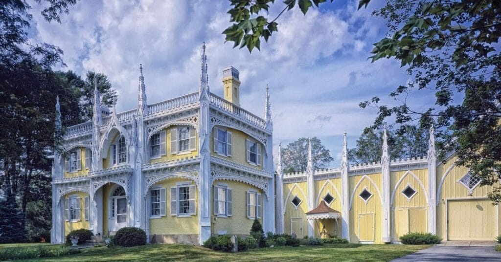 A stunning yellow Gothic Revival-style house surrounded by greenery under a partly cloudy sky, one of the must-see attractions when exploring things to do in Kennebunkport Maine.