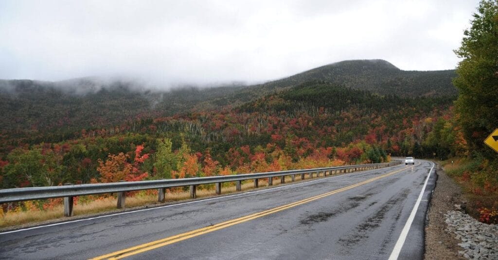 A scenic mountain road surrounded by vibrant fall foliage in North Conway, NH, on a misty day.