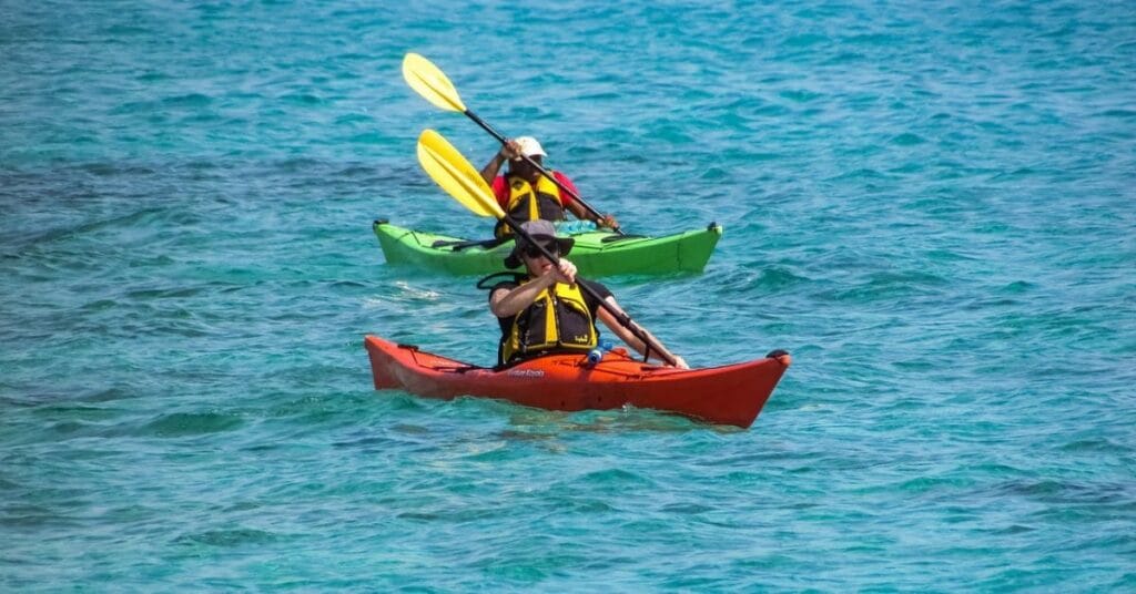 Two people kayaking in the clear blue waters, wearing life jackets and paddling through the waves under a bright sky.