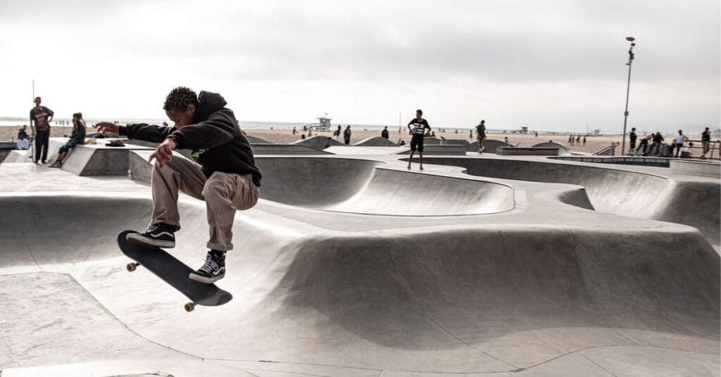 A skateboarder performing a trick at a concrete skatepark near the beach, with onlookers and the ocean in the background—one of the exciting things to do in Miramar Beach.