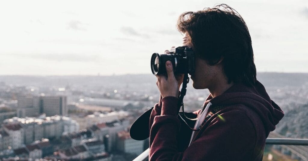 A man using a compact camera to capture a cityscape from a high viewpoint.