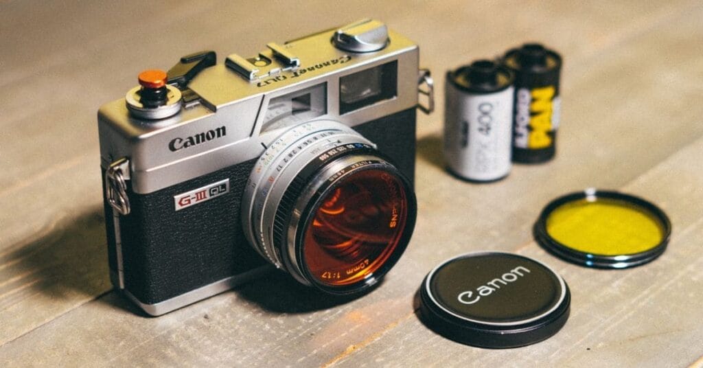 A vintage Canon G-III QL camera with film rolls and accessories on a wooden surface.