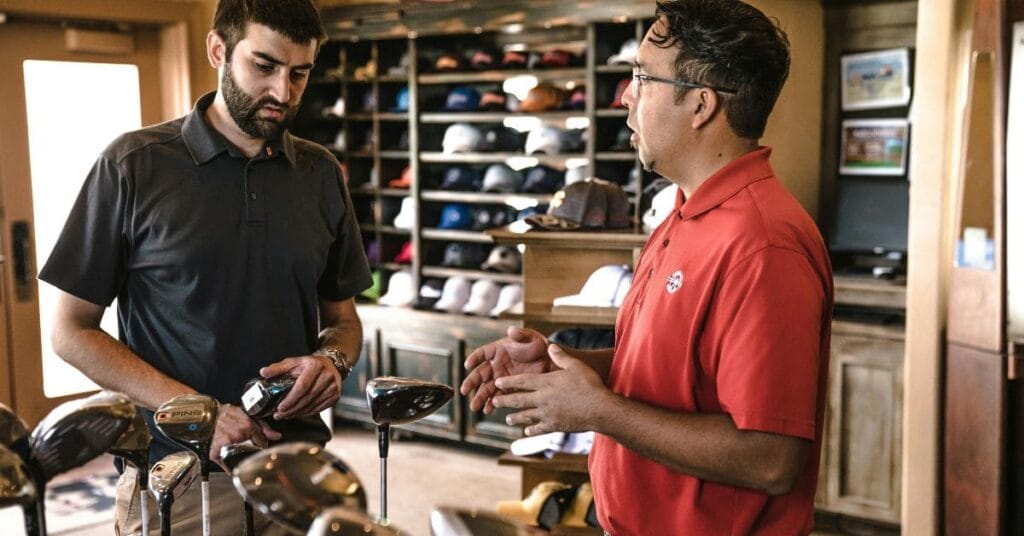 Two men discussing golf clubs in a store, surrounded by various golf equipment and accessories, exploring options for the best golf travel case.