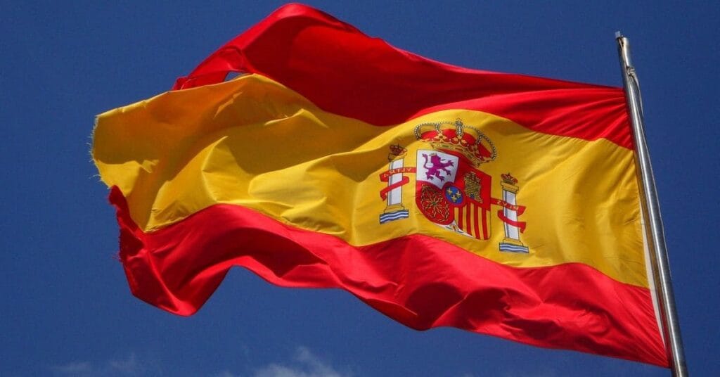 Spanish flag waving against a blue sky, representing travel in Spanish-speaking destinations and Spain's cultural heritage.