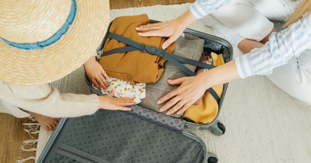 A child and an adult packing a suitcase together with neatly folded clothes and accessories, preparing for travel.