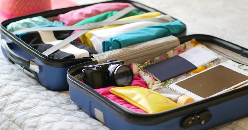 Open suitcase packed with travel essentials for women, including clothes, toiletries, a camera, and a tablet.