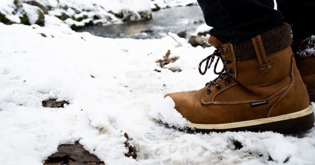 Brown waterproof winter boots on snow near a stream, highlighting their durability for wide-foot winter travel.