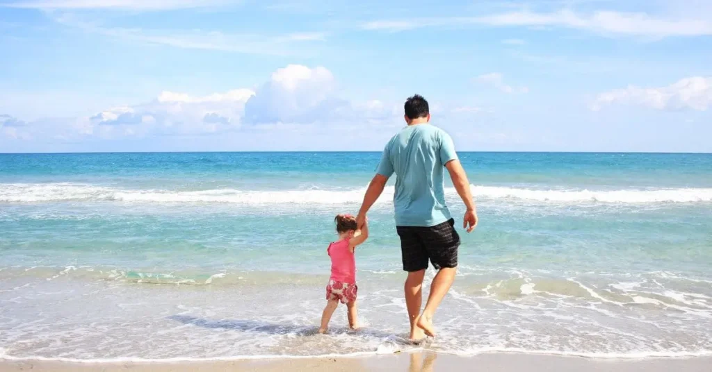 Father and child walking on a sunny beach showcasing one of the best places to travel in July