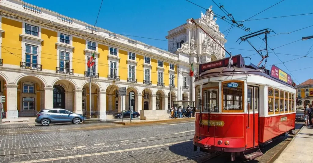 Iconic red tram in Lisbon, Portugal, a vibrant destination for travel as a Black girl, passing by a historic yellow building under a clear blue sky.