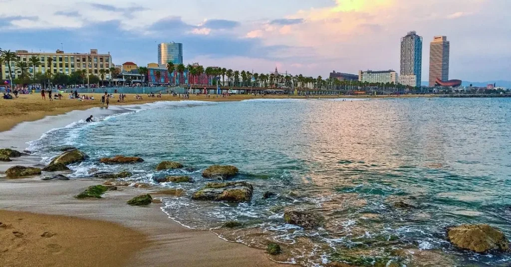 Sunset view of Barceloneta Beach in Barcelona, a perfect spot for travel as a Black girl, with golden sand, clear waters, and the city skyline in the background.