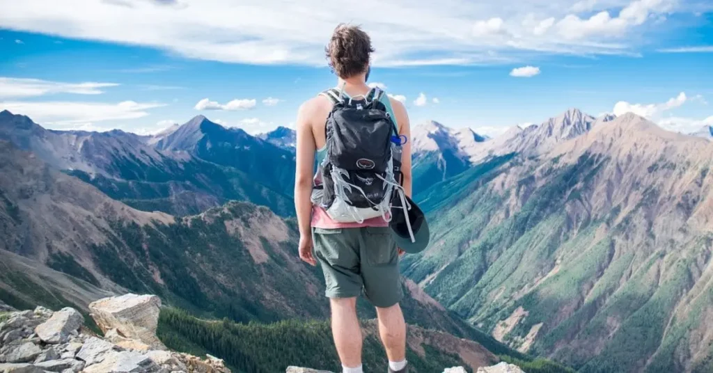 Man wearing an Osprey backpack, gazing at mountains and scenic views during a budget-friendly outdoor adventure.