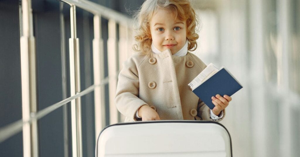 A child holding a passport and standing next to luggage, ready for international travel with family, meeting the child requirement to travel to Pakistan with one parent.