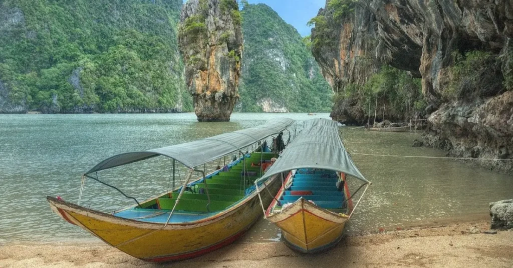 Traditional long-tail boats on a serene beach in Phang Nga Bay, Thailand, with towering limestone cliffs in the background—ideal for exploring during the best time to visit Thailand.