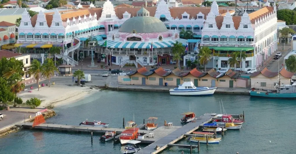 View of the colorful harbor and shops in Oranjestad, Aruba, with boats docked along the pier and vibrant buildings along the waterfront.