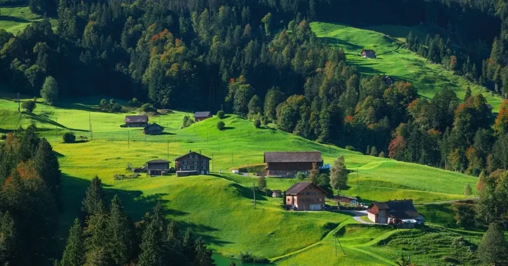 A breathtaking view of Switzerland’s alpine landscape, showcasing lush green valleys, snow-capped mountains, and a serene lake—capturing the beauty of nature during the best time to travel to Switzerland.