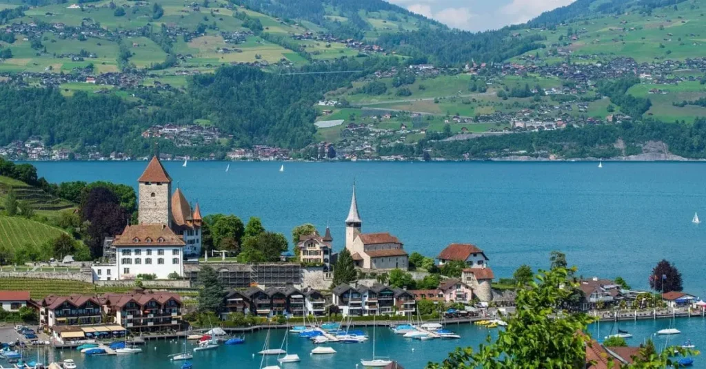 A stunning view of the Swiss village of Spiez, located on the shores of Lake Thun, surrounded by lush green hills and the majestic Swiss Alps—capturing the beauty of nature during the best time to travel to Switzerland.