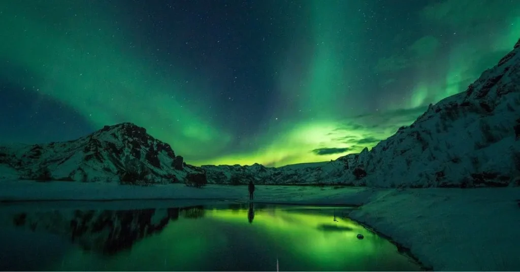 The best time to visit Alaska to see northern lights is during the winter months, as two people stand beneath the vibrant aurora borealis dancing across the night sky.