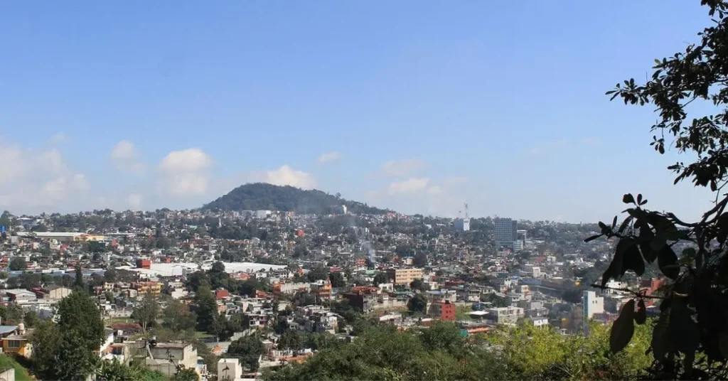 A panoramic view of a city with a prominent hill, Cerro de Macuiltepetl, rising in the center, showcasing the urban landscape nestled amidst natural beauty.