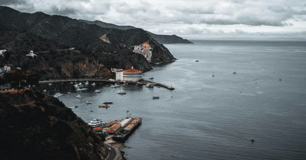 A scenic aerial view of Avalon Harbor on Catalina Island, showcasing the bay filled with boats, the iconic Casino building, and the surrounding hills. This image highlights the beauty and suggests catalina island things to do for visitors.