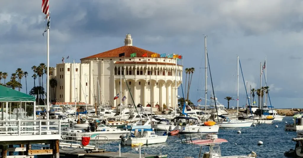 A close-up view of the Catalina Casino, a large round building with a red tile roof, surrounded by numerous sailboats and palm trees, showcasing a key attraction and things to do on Catalina Island.