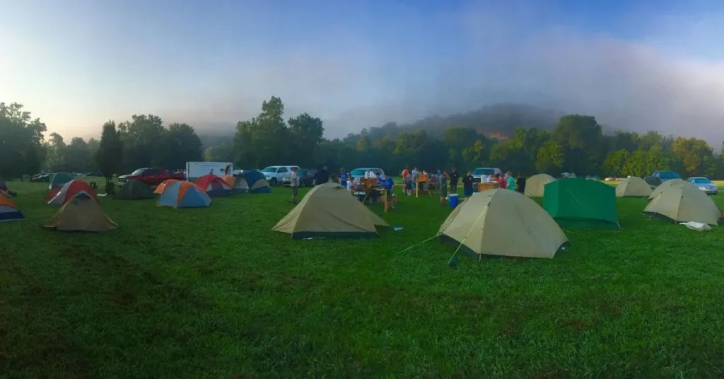 A wide shot of a misty campsite with various tents and people gathered, representing the spirit of adventure and outdoor exploration, similar to scouting related places to visit in Japan, where nature and cultural immersion go hand-in-hand.