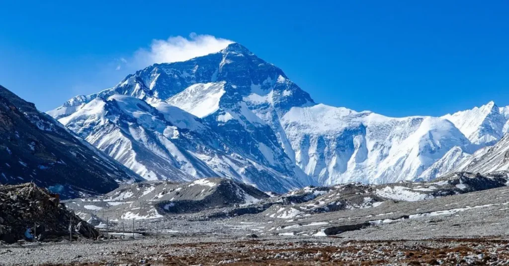 A stunning view of Mount Everest's peak with a plume of snow blowing off it under a bright blue sky, raising the question: what is the best hour to visit Mount Everest for optimal viewing?