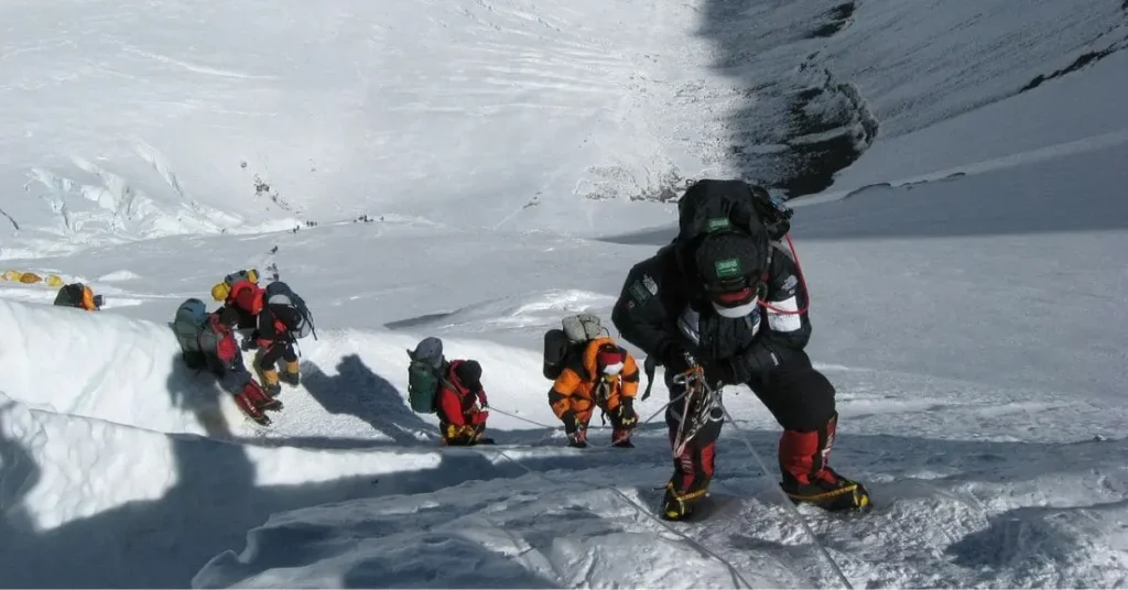 Climbers ascending a steep, icy slope on Mount Everest, using ropes for support. Discover what is the best hour to visit Mount Everest for safe and successful climbing.