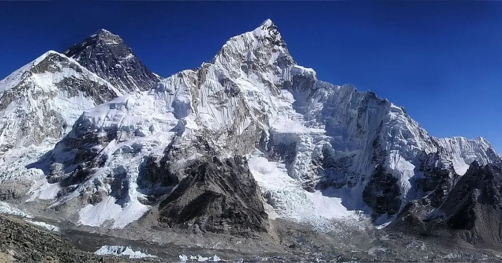 A majestic view of Mount Everest and a neighboring peak, showcasing its snow-covered summit and rugged terrain, illustrating two reasons to visit Mount Everest: for its unparalleled natural beauty and the ultimate mountaineering challenge.