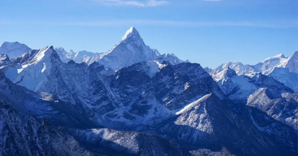 A stunning panoramic view of the Himalayas with a prominent, pointed peak among a range of snow-covered mountains, illustrating two reasons to visit Mount Everest: for its breathtaking natural beauty and the unparalleled adventure it offers.