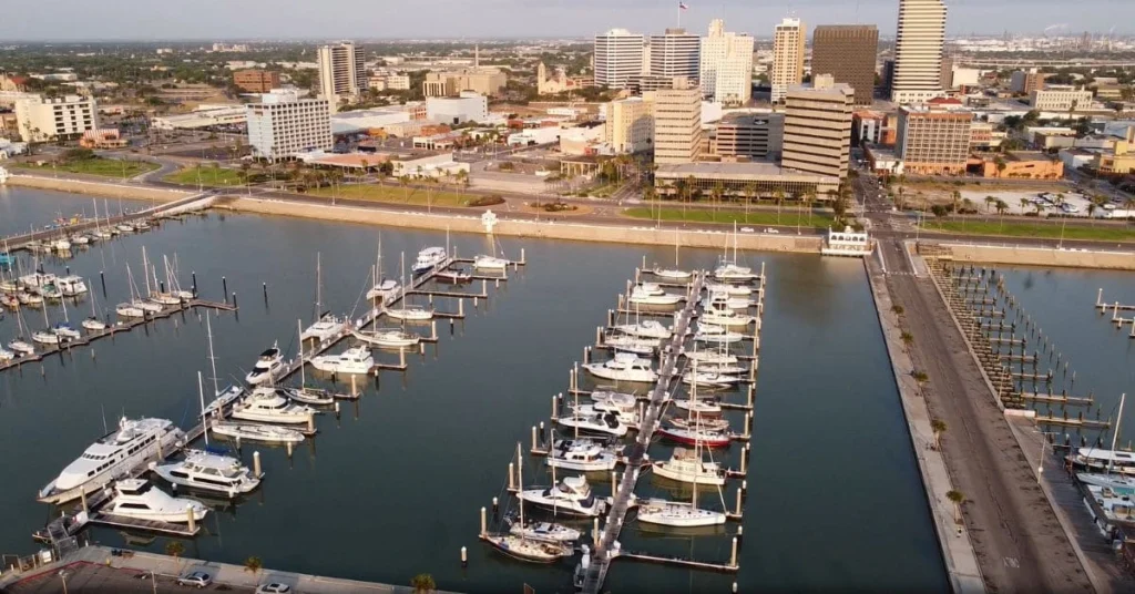 An aerial view of the Corpus Christi Marina with numerous boats docked, showcasing the city skyline in the background, highlighting the proximity to family-friendly accommodations and activities, making it a desirable location when looking for the best hotels for families in Corpus Christi Texas.