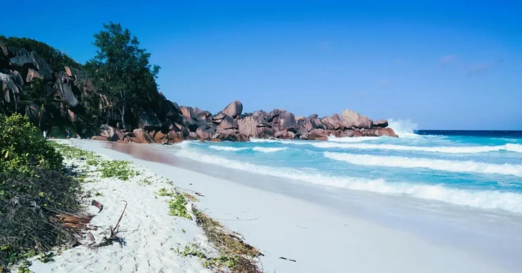 A tranquil beach scene in the Seychelles, with white sand, turquoise waves, and unique rock formations, highlighting one of the most idyllic tropical places to visit.