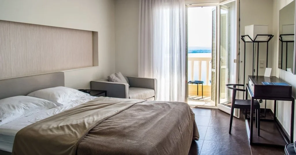 A bright and airy hotel room with a comfortable bed, a small seating area, and a balcony overlooking a sea view, showcasing a relaxing and scenic accommodation.