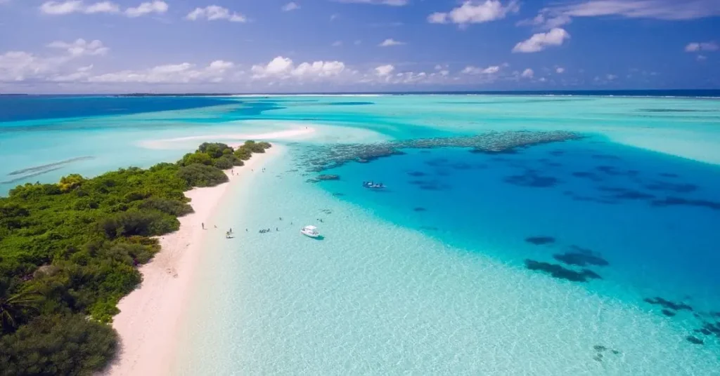 An aerial view of a stunning Maldives atoll, showcasing crystal-clear turquoise waters, a white sand beach, and lush greenery, making it one of the most desirable tropical places to visit.