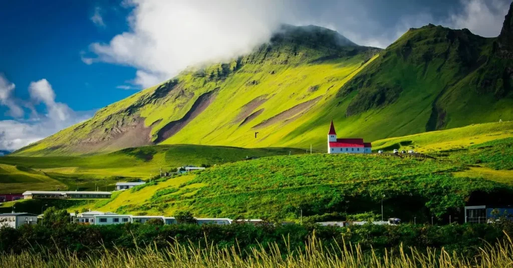 Scenic landscape of Vik, Iceland, with a red-roofed church on a green hillside, illustrating the best time to visit Iceland for vibrant summer views.