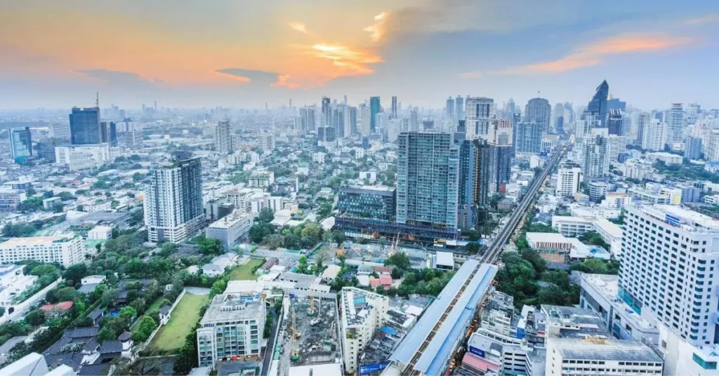 High-angle shot of Bangkok, Thailand, featuring a dense cityscape with numerous high-rise buildings, green spaces, and the elevated BTS Skytrain tracks, highlighting a modern and vibrant city in one of the best asian countries to visit.