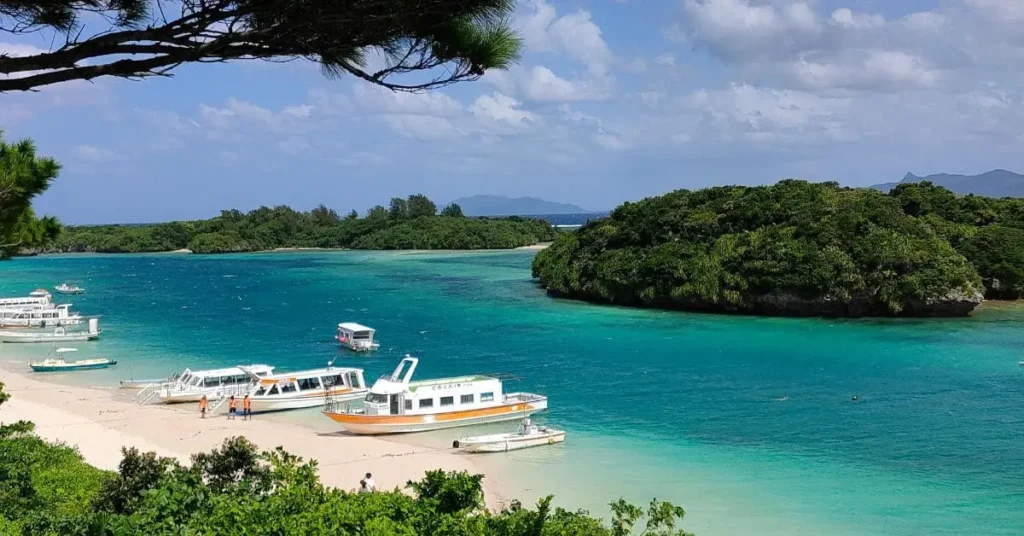 Overhead shot of Kabira Bay, Ishigaki Island, Japan, highlighting white sand beach, multiple tour boats, clear turquoise water, and densely forested islands in the bay, representing a must-see location in the best asian countries to visit.